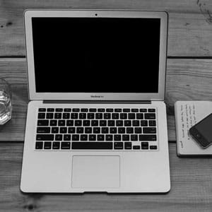 Modern MacBook laptop on wooden desk with notepad and smartphone, representing professional digital workspace.